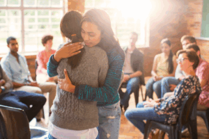 Two women embracing during group therapy session, representing emotional support and healing at Rooted Stillness in Newport Beach