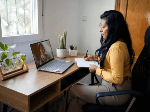 Woman attending virtual therapy session on laptop and taking notes, representing virtual IOP and personalized mental health care at Rooted Stillness in Newport Beach