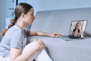 Woman attending virtual therapy session from home on laptop, representing virtual IOP and accessible mental health care at Rooted Stillness in Newport Beach
