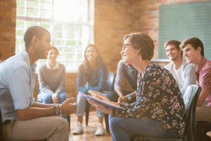 Therapist leading group counseling session with clients, representing supportive mental health and addiction treatment at Rooted Stillness in Newport Beach