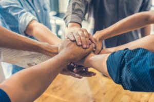 Group of diverse hands together representing peer support, connection, and not being alone in recovery at Rooted Stillness virtual IOP in Newport Beach.