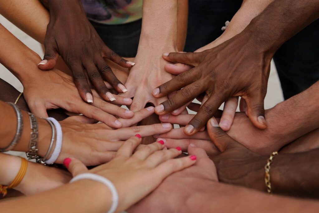 Group of diverse hands together representing peer support, connection, and not being alone in recovery at Rooted Stillness virtual IOP in Newport Beach.