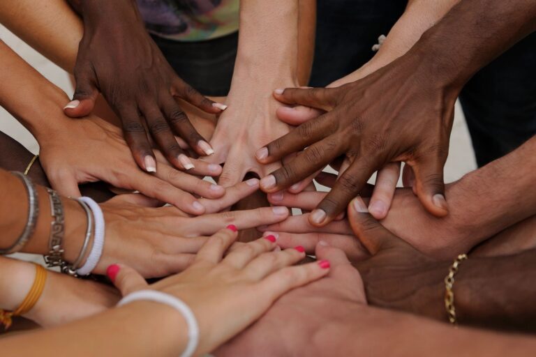Group of diverse hands together representing peer support, connection, and not being alone in recovery at Rooted Stillness virtual IOP in Newport Beach.