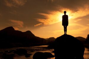 Silhouette of person standing on rock at sunset symbolizing healing and personal growth at Rooted Stillness virtual IOP in Newport Beach.