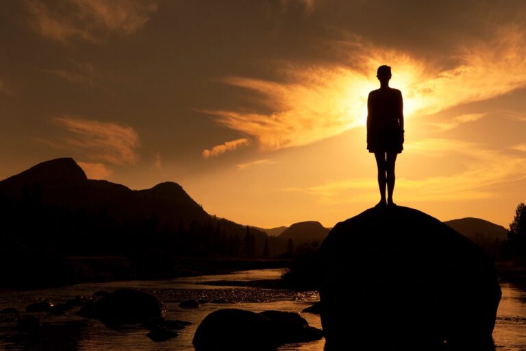 Silhouette of person standing on rock at sunset symbolizing healing and personal growth at Rooted Stillness virtual IOP in Newport Beach.